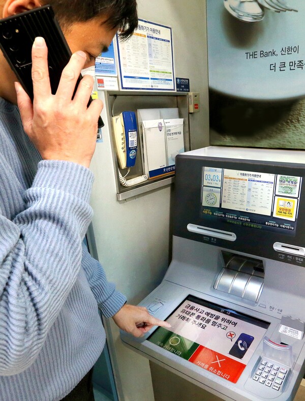 [▲핸드폰으로 통화하며 신한은행 ‘AI 이상행동탐지 ATM’을 이용하고 있는 도중 ATM 화면에 금융사고 예방 주의 문구가 나오는 모습 = ©신한은행]