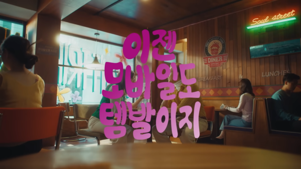 [AP신문광고평론 No.625]  레트로한 분위기의 카페에 앉아있는 두 모델. 사진 KT M모바일 유튜브 캡처 ⓒAP신문