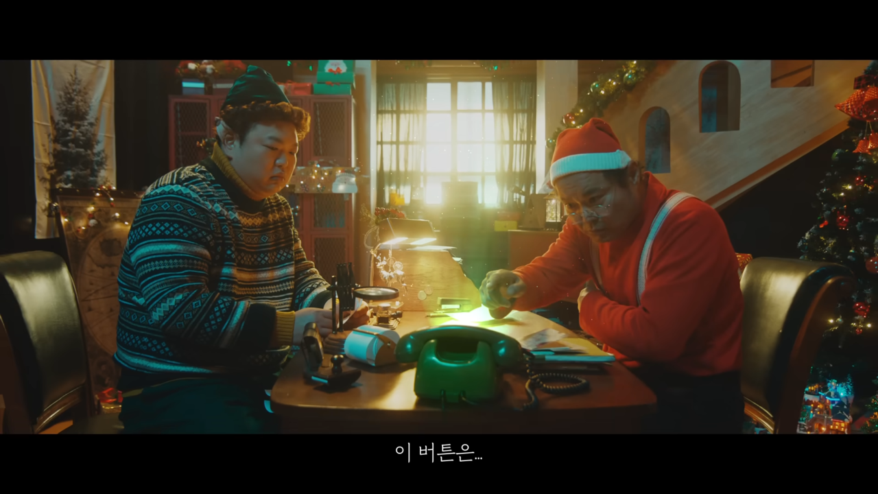 [AP신문 광고평론 No.701] 전화기의 G버튼을 바라보는 산타(김상호)와 그의 조수(고규필). 사진 G마켓 유튜브 캡처 ⓒAP신문