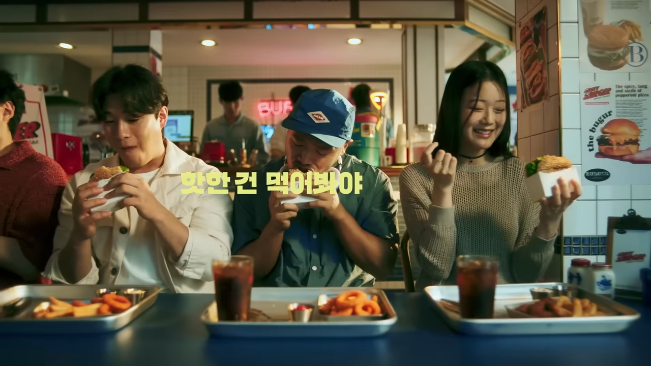 [AP신문 광고평론 No.1054]  ​​​​​​​햄버거 맛집에서 햄버거를 먹고 있는 젊은 사람들. 사진 SSG.COM 유튜브 캡처 ⓒAP신문(AP뉴스)